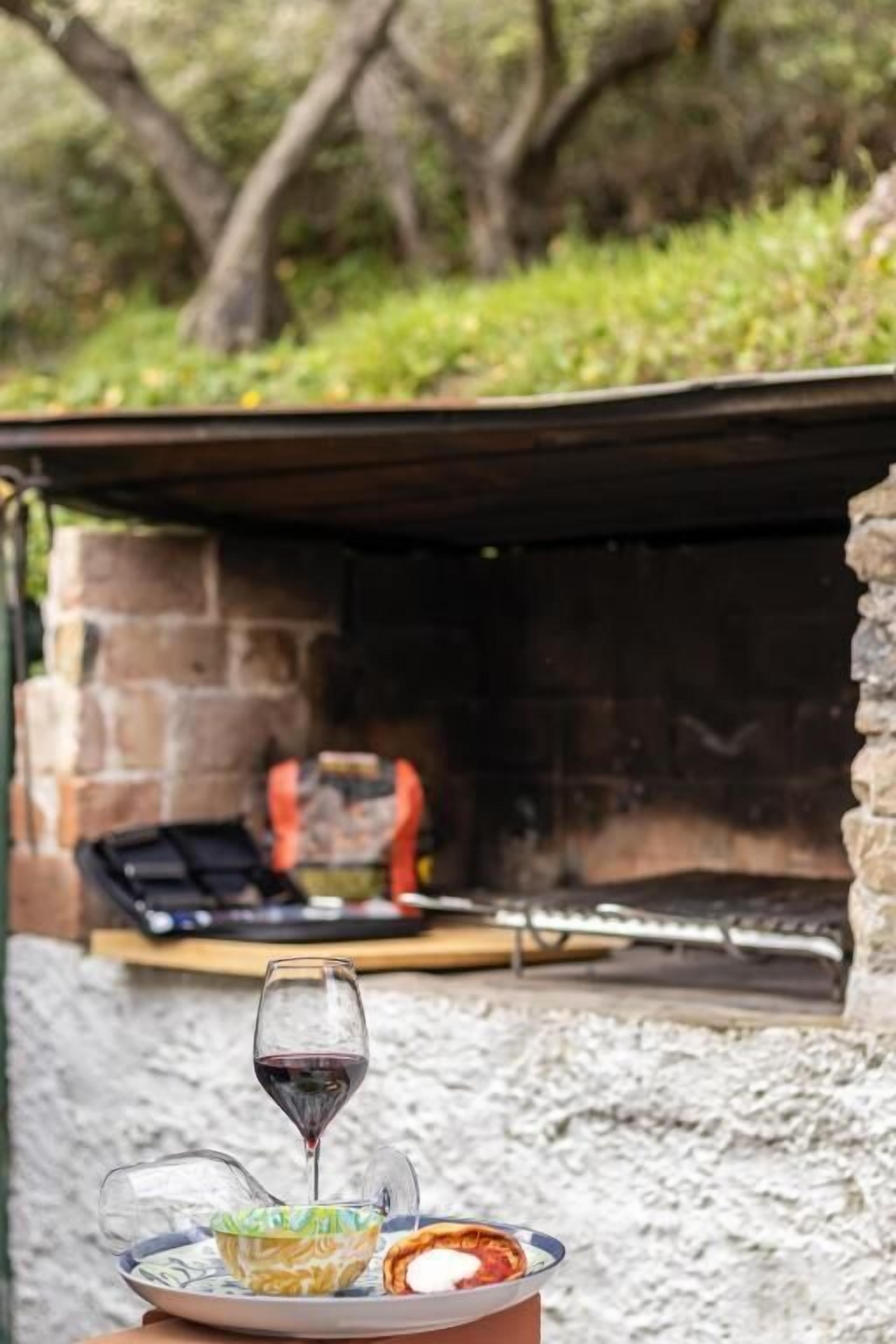 Uma lareira de pedra com grelha, um copo de vinho tinto e um prato com comida e uma tigela.