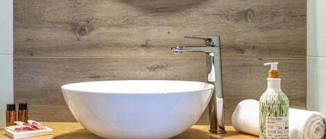Un baño con un lavamanos blanco tipo recipiente, un grifo moderno, una botella de jabón y una toalla en la encimera.