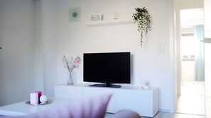 A modern living room with a flat-screen TV on a white console, a vase with orchids, and a hanging plant. - Holiday Apartment for 4 Guests (70 m²) in Boos (Mayen-Koblenz) (Boos)
