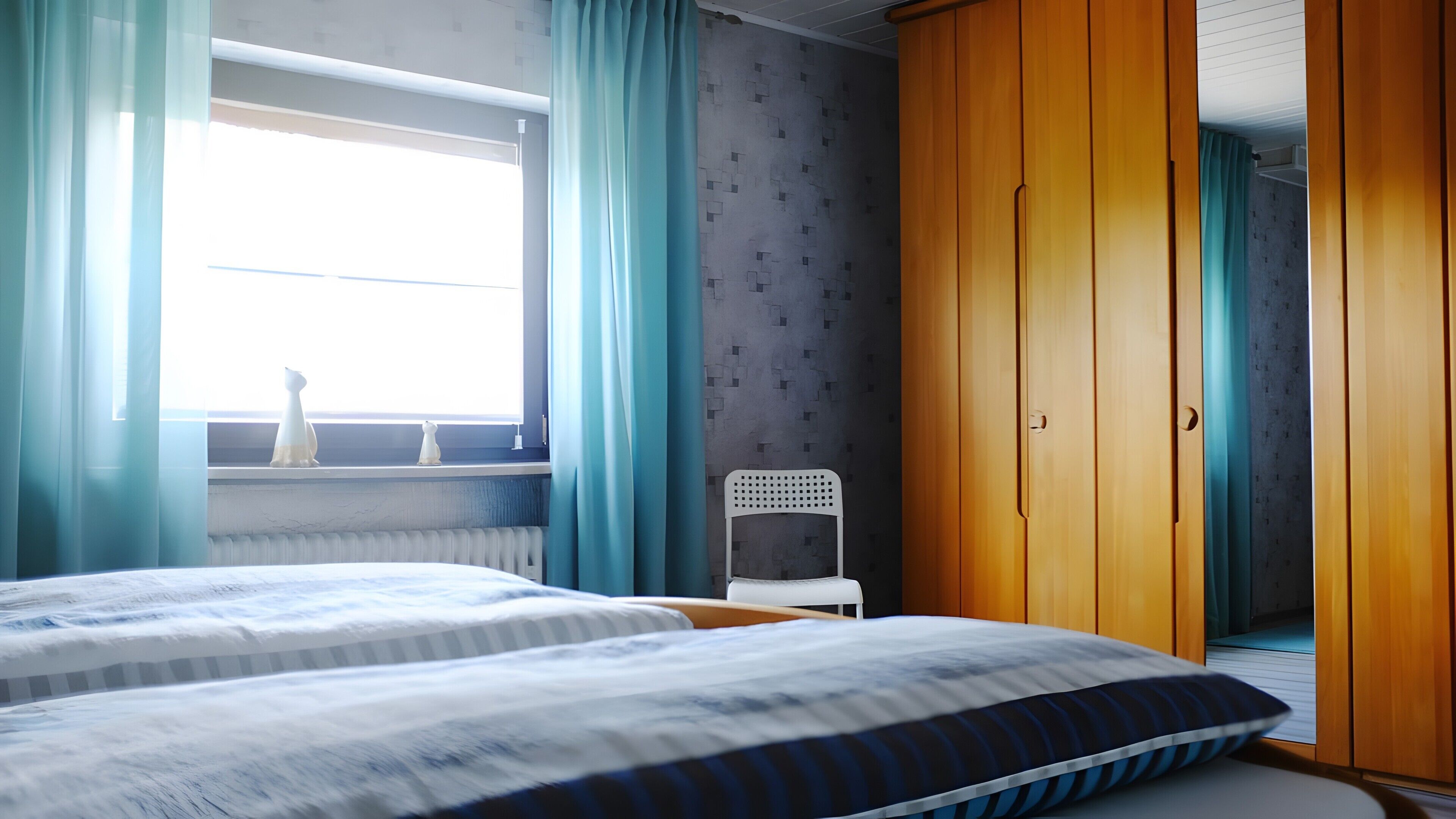 Une chambre avec deux lits, une fenêtre avec des rideaux, un radiateur, une chaise blanche et des armoires en bois.