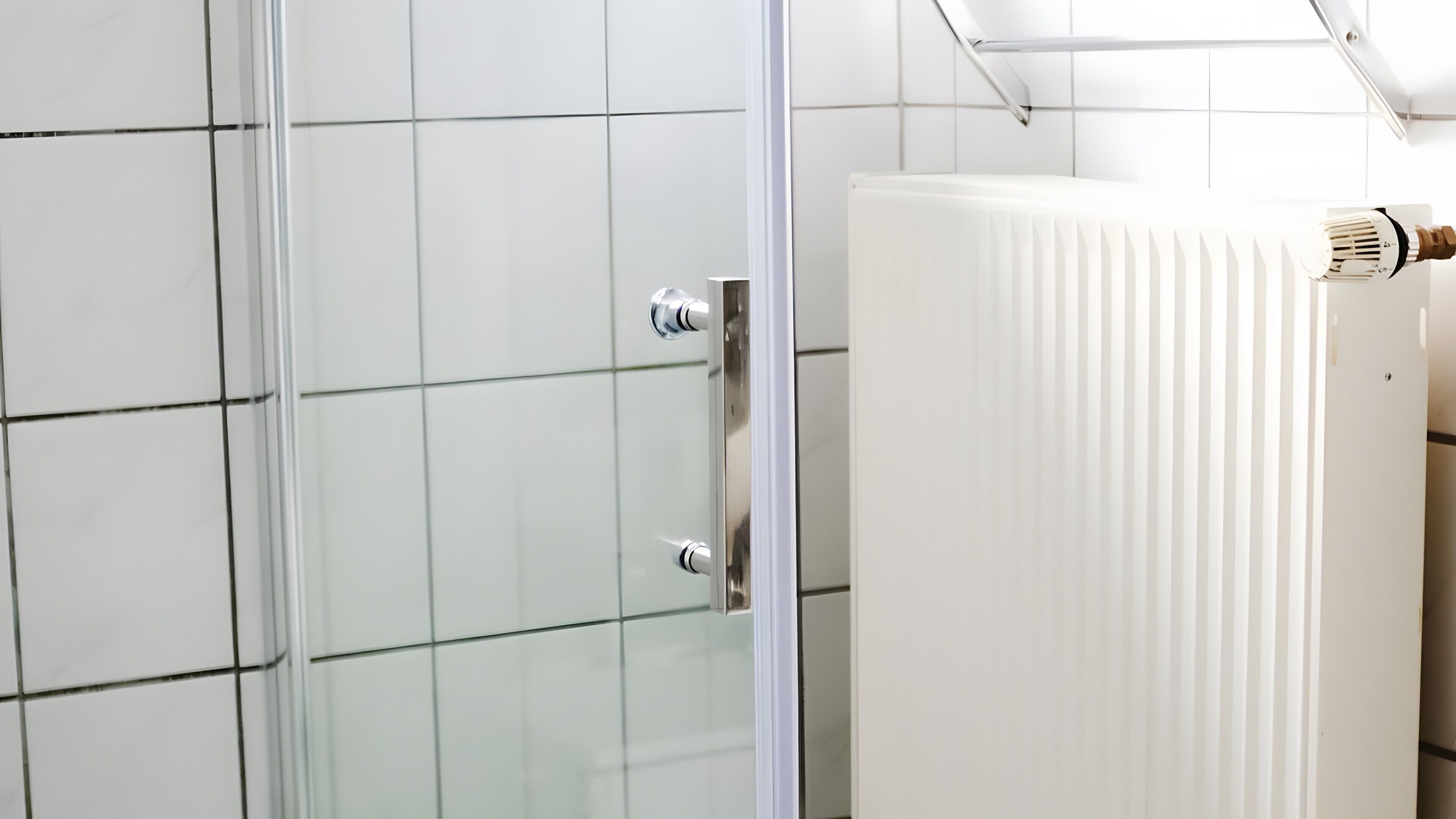A bathroom with white tiled walls, a glass shower enclosure, and a white radiator.