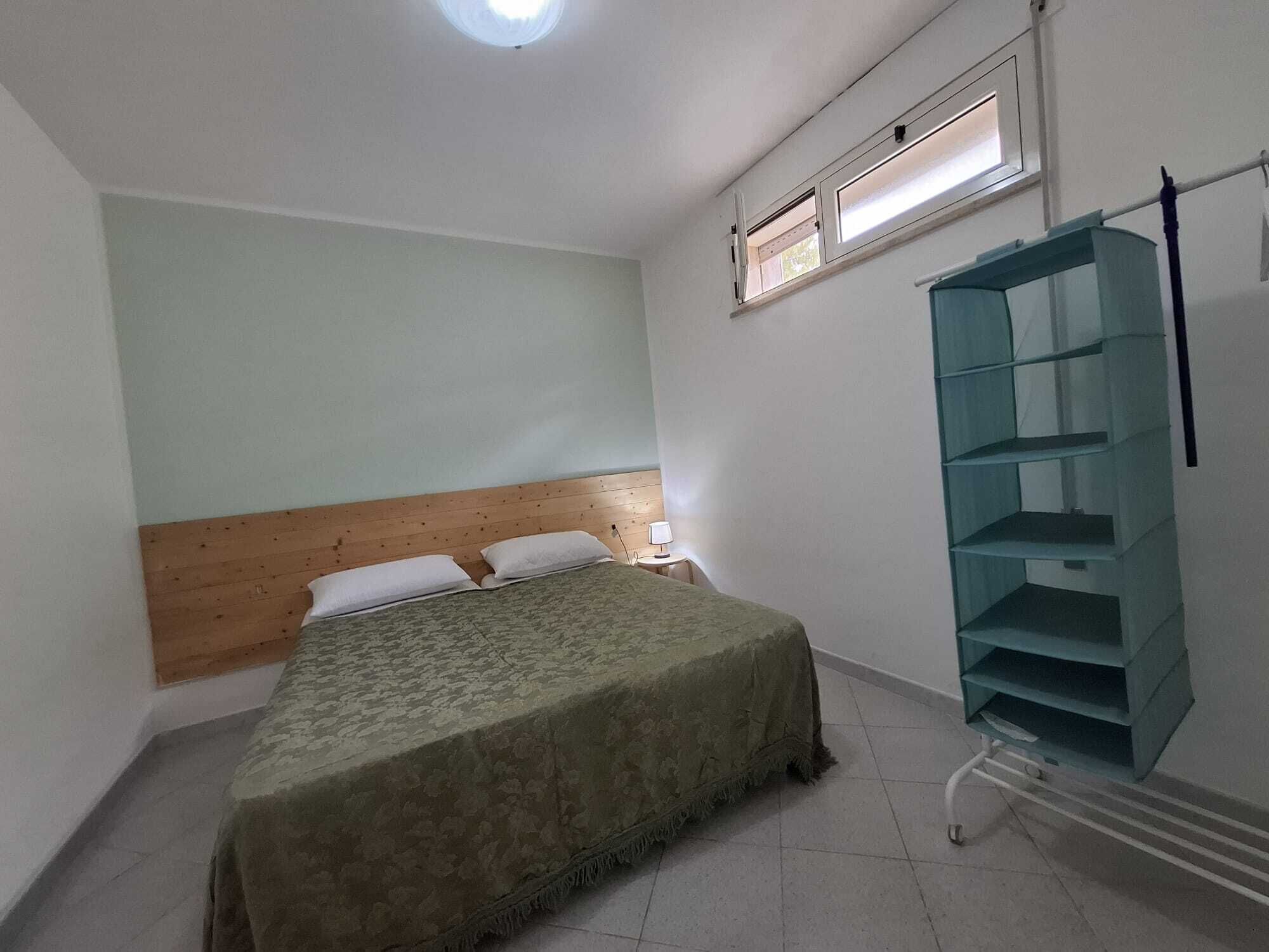 Een slaapkamer met een bed, nachtkastje, raam met zonwering en een inbouwkast.