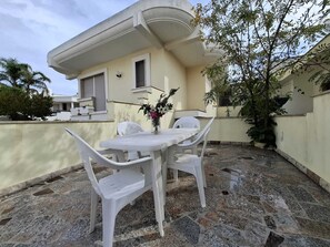 Eine Terrasse mit Tisch und Stühlen, einer Blumenvase und einem Gebäude im Hintergrund.