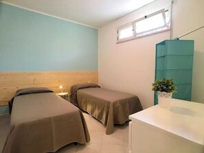 Ein Zimmer mit zwei Einzelbetten, einem kleinen Nachttisch, einem Spiegel und einem Fenster.