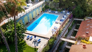 Ein Pool mit Liegestühlen und Sonnenschirmen, umgeben von Grünflächen und Gebäuden.