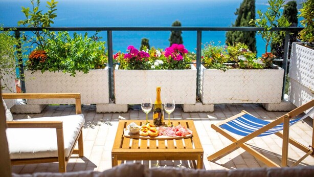 Eine Terrasse mit Holztisch, zwei Stühlen, einer Weinflasche und einem Glas.