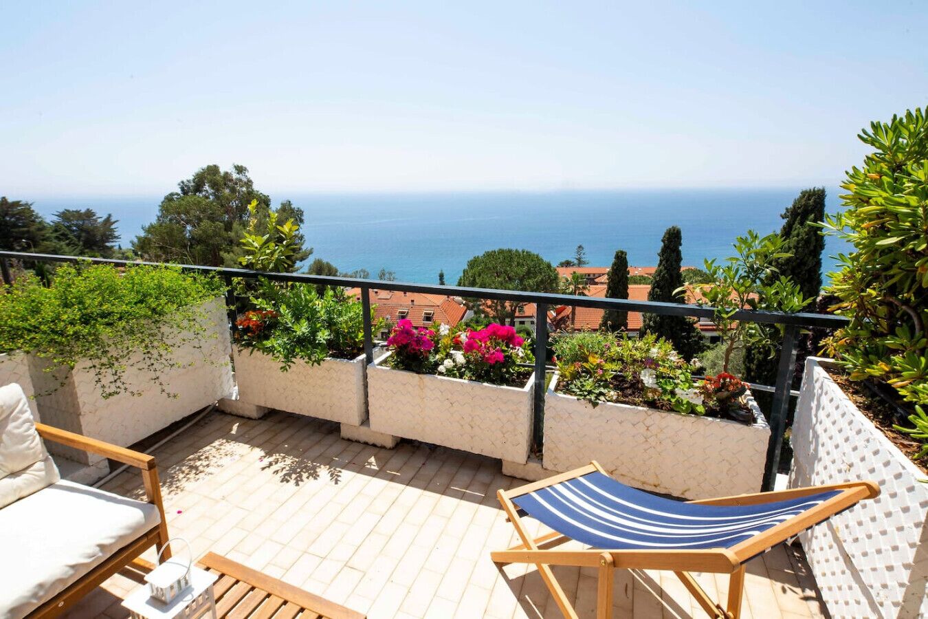Un balcon avec vue sur la mer, des meubles en bois et des plantes en pot.