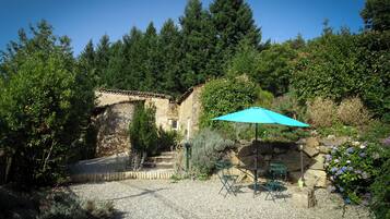 A rustic stone building with a gravel patio, outdoor seating, and a blue umbrella.