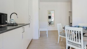 A modern kitchen with a microwave, kettle, and kettle stand. There is a dining area with a table and chairs. - Tuscolana Costantino's Apartment by Rentbeat (Roma)