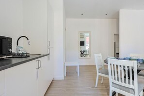 A modern kitchen with a microwave, kettle, and kettle stand. There is a dining area with a table and chairs. - Tuscolana Costantino's Apartment by Rentbeat (Roma)
