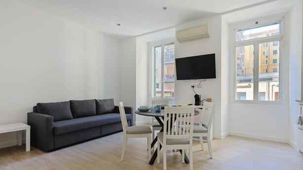 A modern living room with a grey sofa, white chairs, a dining table, and a TV mounted on the wall. - Tuscolana Costantino's Apartment by Rentbeat (Roma)