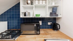 A kitchen with a gas stove, a microwave, a kettle, and a cabinet with dishes and cups. - New! Bright Brixton 1BR | Walk to Market & Tube (Greater London)