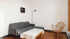 A room with a grey sofa, a wooden chair, a small table with a white tablecloth, a floor lamp, and a picture on the wall. - New! Bright Brixton 1BR | Walk to Market & Tube (Greater London)