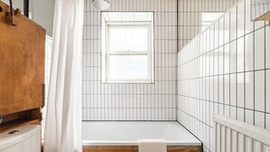 A bathroom with a bathtub, a window, and wooden paneling. - New! Bright Brixton 1BR | Walk to Market & Tube (Greater London)