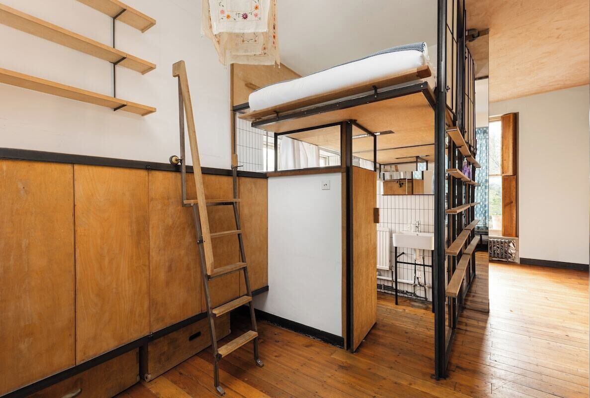 A room with a loft bed, wooden flooring, a ladder, and a white radiator.