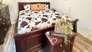 Quarto com cama de madeira, mesa de cabeceira, penteadeira e teto com vigas aparentes.