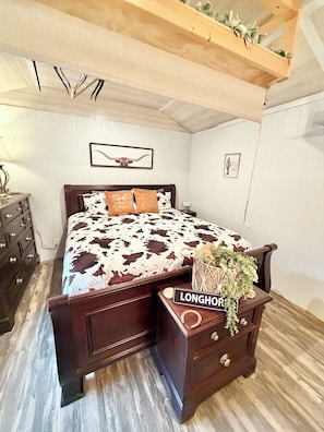 Een slaapkamer met een houten bed, nachtkastje, dressoir en een plafond met zichtbare balken.