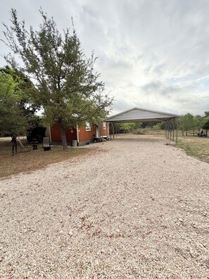 A gravel driveway leading to a covered outdoor area with a wooden building and a large tree.