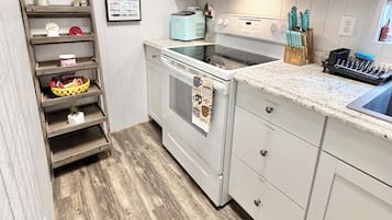 Una cocina con armarios blancos, microondas, tostadora y piso de madera.