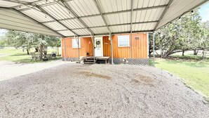 Un espacio al aire libre techado con suelo de grava, bancos de madera y una estructura de techo metálico.