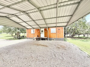 A covered outdoor area with a gravel floor, wooden benches, and a metal roof structure.