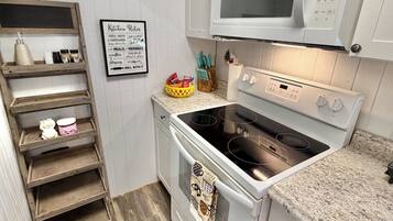 A compact kitchen with a microwave, oven, and a wooden shelf unit.