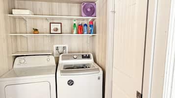 A laundry room with a washing machine, dryer, shelves with cleaning supplies, and a fan.