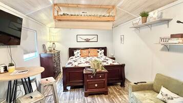 A bedroom with a bed, a desk, a chair, a nightstand, a sofa, a ceiling fan, and a TV.