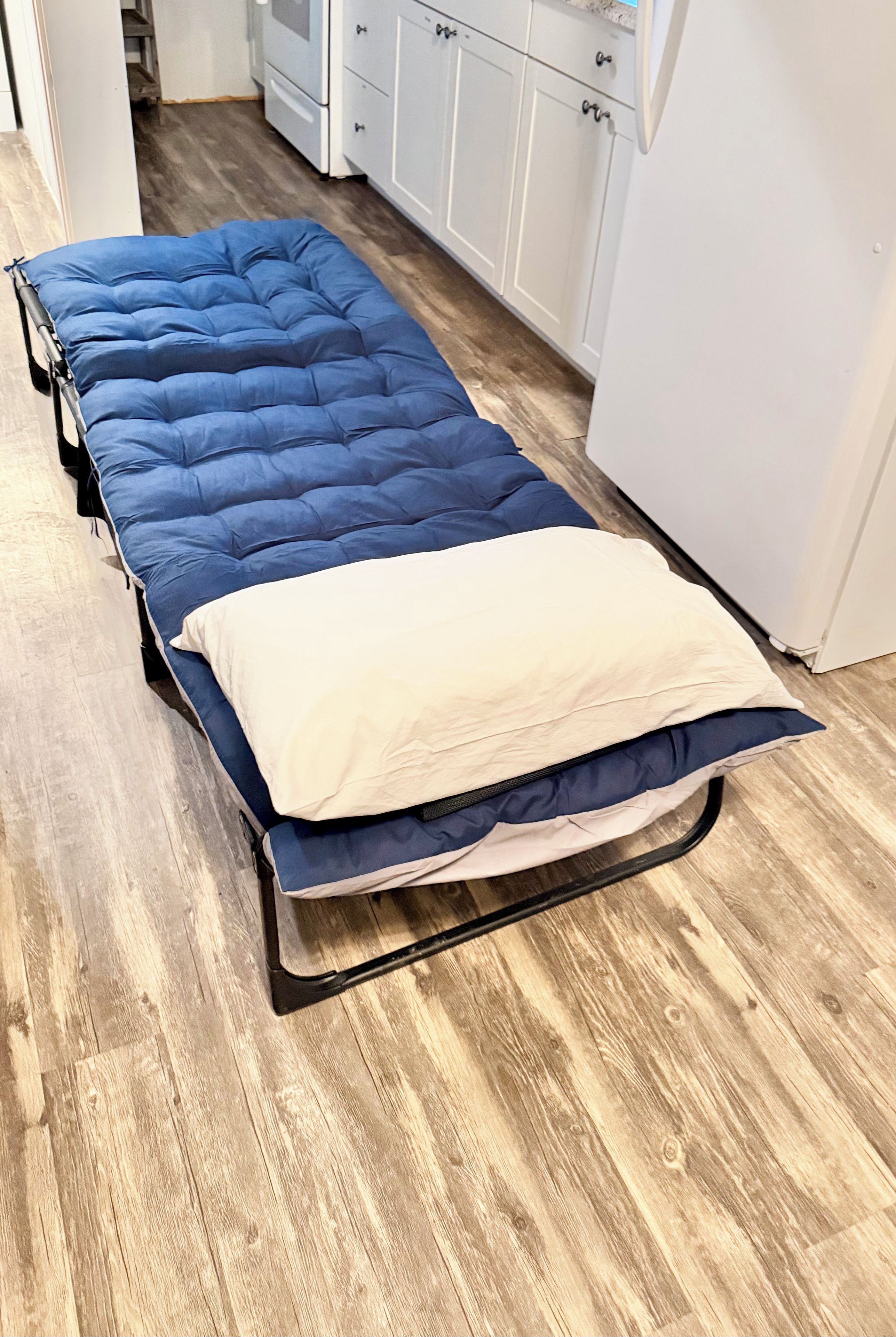 A single bed with a blue mattress and a white pillow in a room with wooden flooring and white cabinetry.
