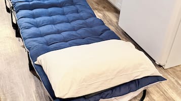 A single bed with a blue mattress and a white pillow in a room with wooden flooring and white cabinetry.