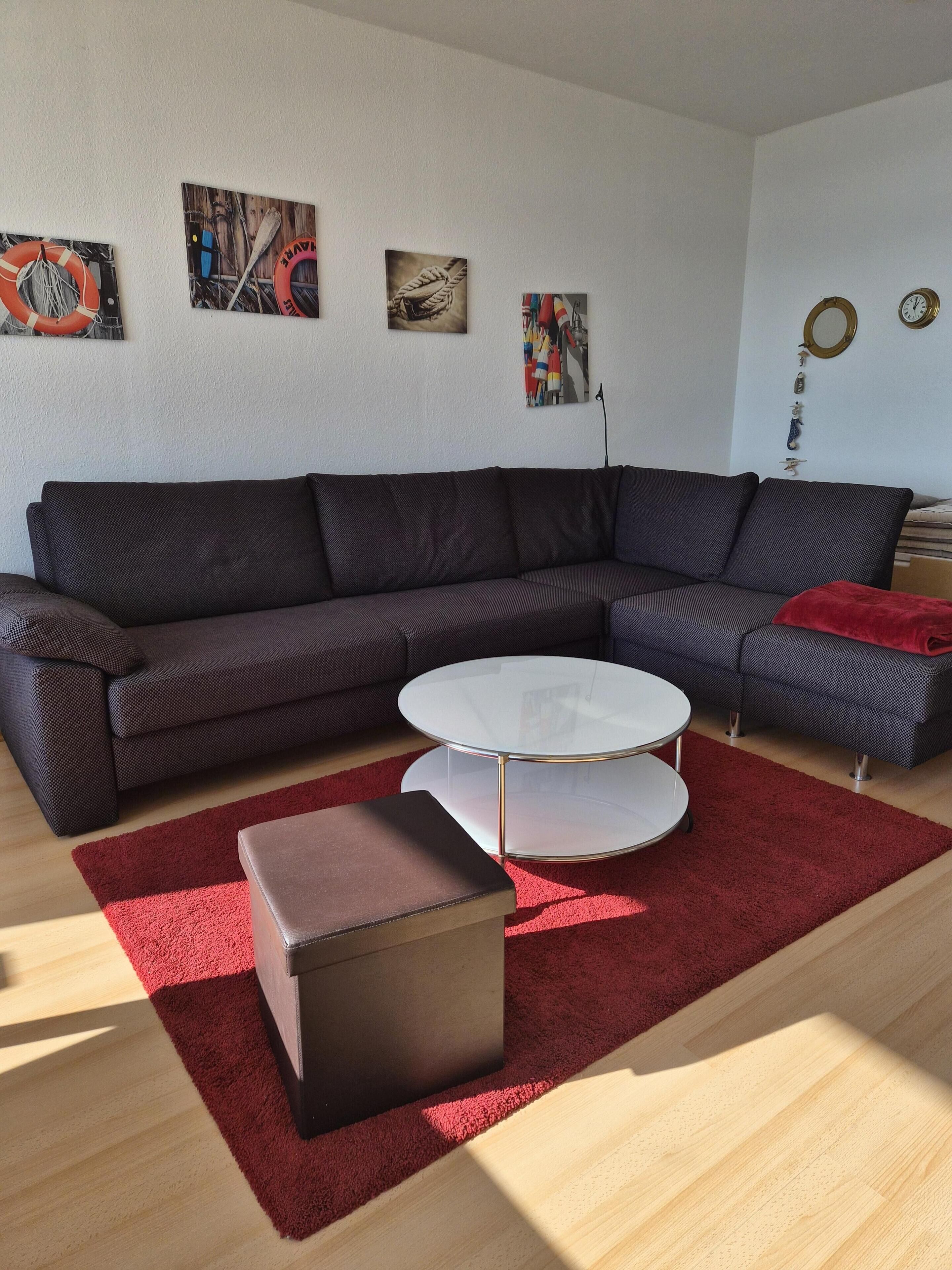 Ein modernes Wohnzimmer mit einem Ecksofa, einem Glastisch, einem roten Teppich und Wandbildern.