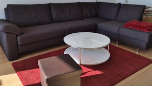 Ein modernes Wohnzimmer mit einem Ecksofa, einem Glastisch, einem roten Teppich und Wandbildern.