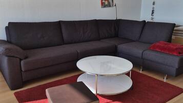 Ein modernes Wohnzimmer mit einem Ecksofa, einem Glastisch, einem roten Teppich und Wandbildern.