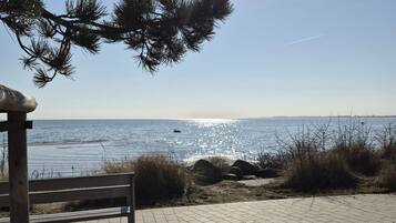 Ein gepflasterter Weg führt zu einem Strand, auf der linken Seite befindet sich eine Holzkonstruktion.
