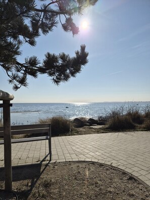 A paved walkway leading to a beach with a wooden structure on the left. - Four Seasons 4-40 - Großenbrode (Großenbrode)
