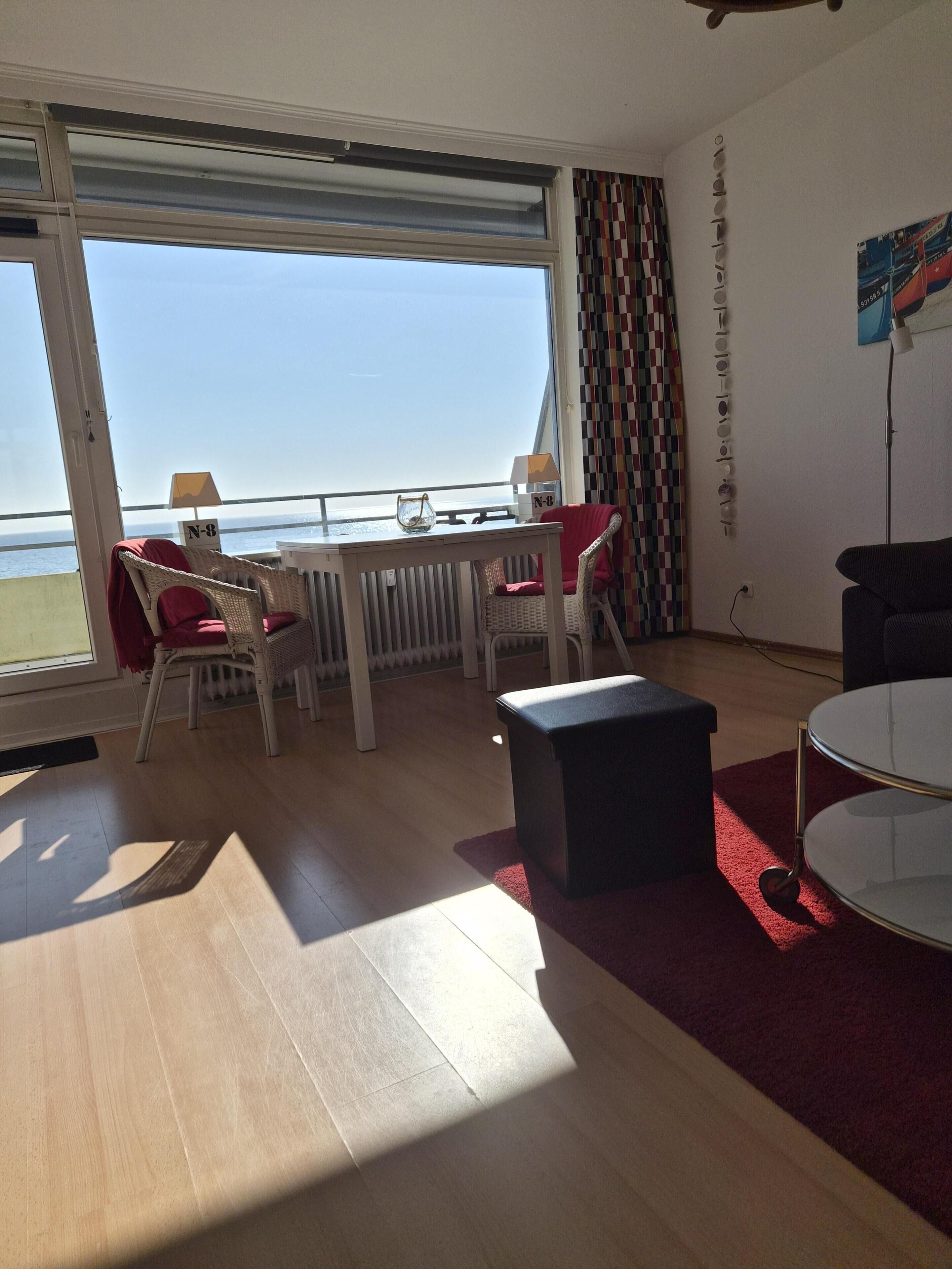 Ein Zimmer mit großem Fenster, einem Tisch mit Stühlen, einer kleinen Couch und einem runden Tisch.