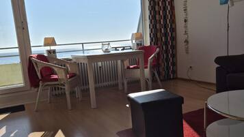 Ein Zimmer mit großem Fenster, einem Tisch mit Stühlen, einer kleinen Couch und einem runden Tisch.