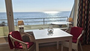 Ein Zimmer mit Tisch und Stühlen, Blick aufs Meer und einem Vorhang vor dem Fenster.