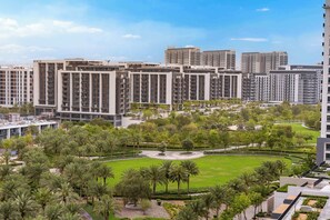 A high-rise residential building with multiple balconies, a well-maintained lawn with palm trees, and a clear sky. - StayShort - Dubai Hills - Premium 2BR with Sunlit Balcony - Sleeps 4 (Dubai Hills Estate)