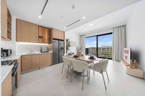 A modern kitchen with wooden cabinets, a built-in oven, and a dining area with a round table and chairs. - StayShort - Dubai Hills - Premium 2BR with Sunlit Balcony - Sleeps 4 (Dubai Hills Estate)