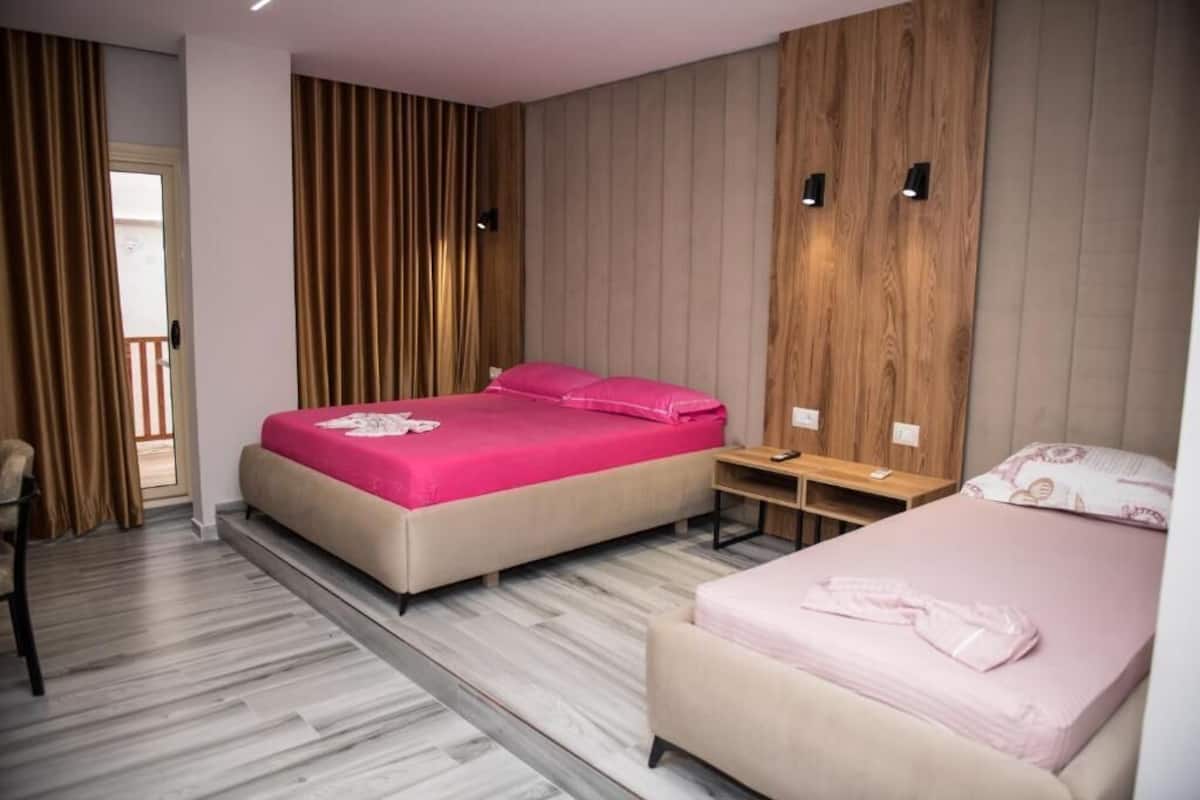A bedroom with two beds, a wooden wall panel, a small table, and a chair.