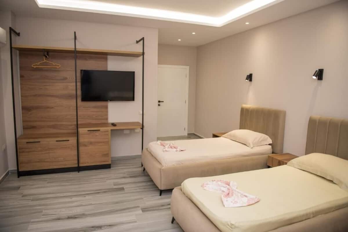 A hotel room with two beds, a TV mounted on a wooden panel, a wardrobe, and a door.