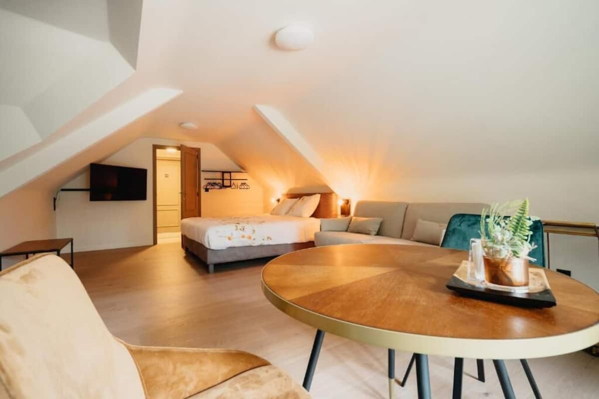 A modern loft bedroom with a sloped ceiling, a round dining table, and a view of the city.