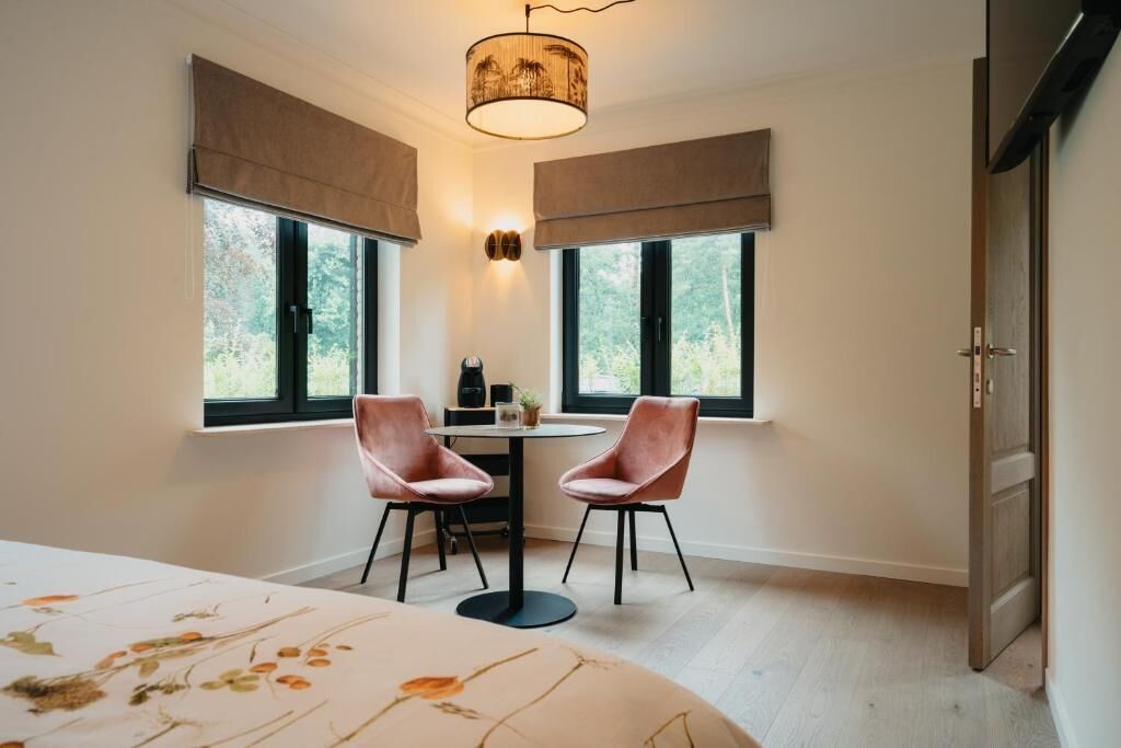 Een kamer met twee stoelen, een tafel, een bed en een raam met uitzicht op bomen.