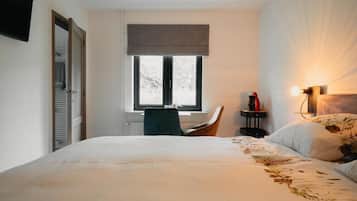 Un dormitorio con cama, una silla, un ventanal, una mesita de noche con lámpara y un televisor montado en la pared.