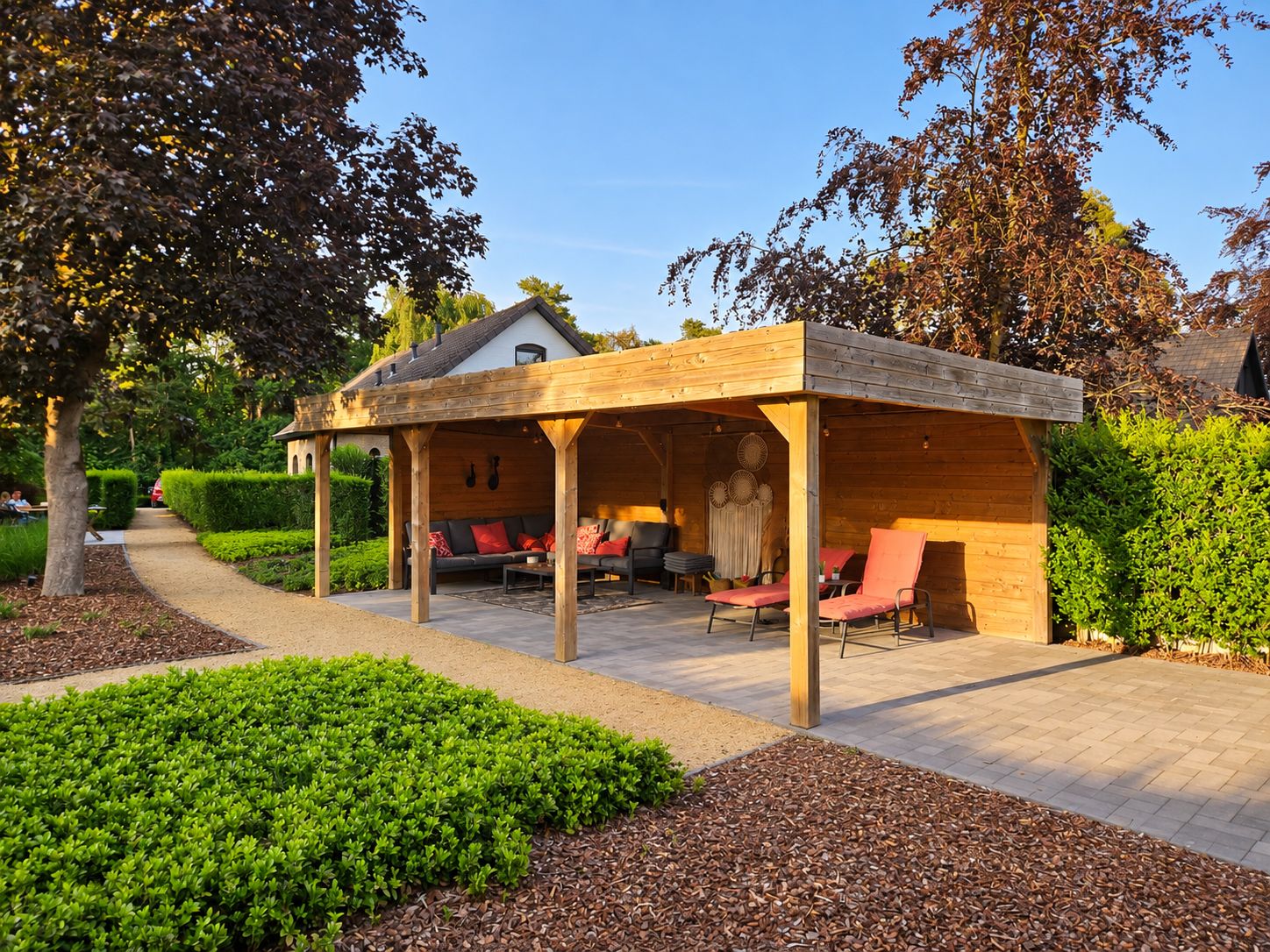 Een overdekt terras met houten constructie, een pad en verzorgde beplanting.