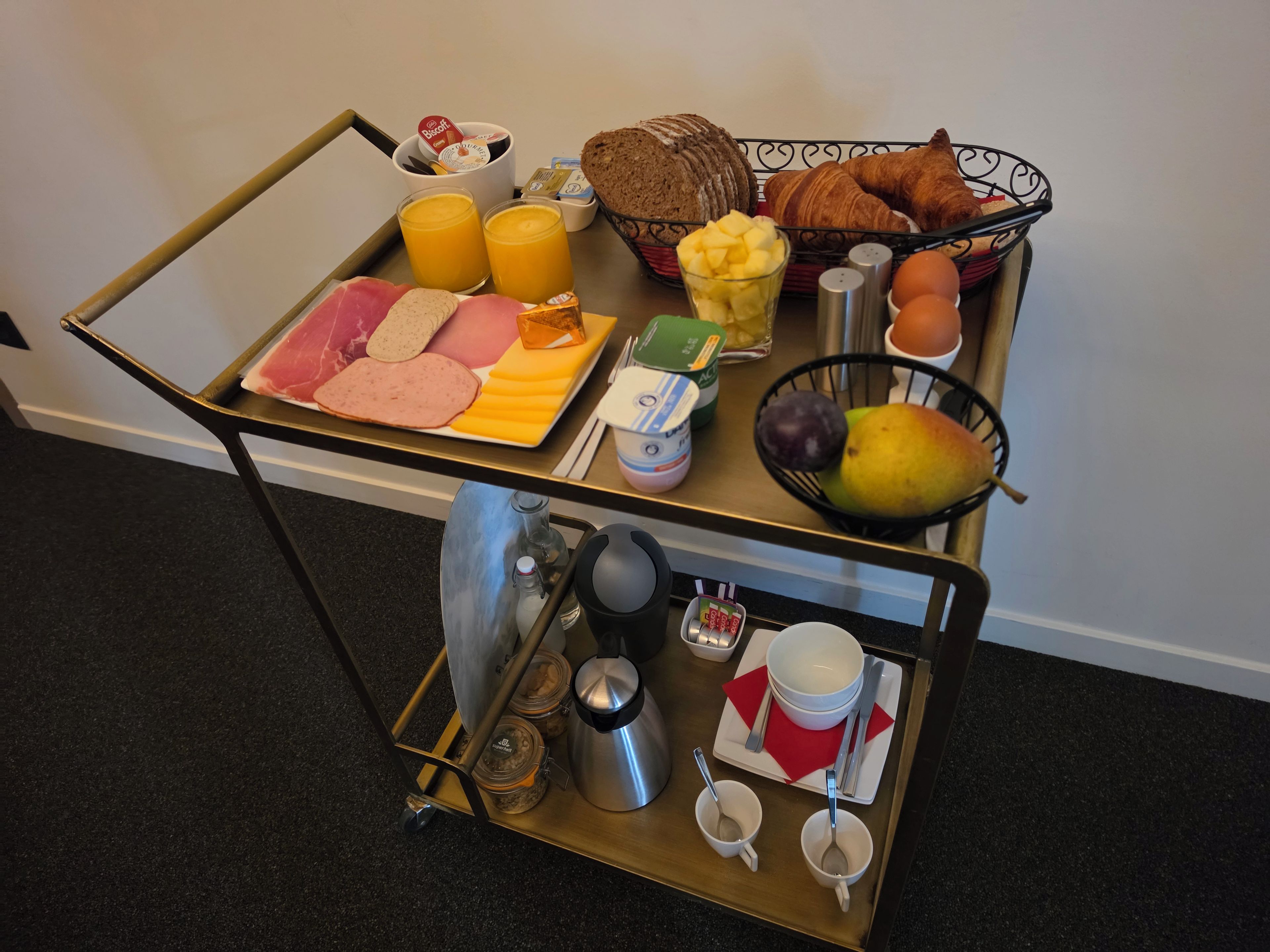 Un carrito de desayuno con diversos alimentos, como pan, bollería, frutas y salsas.