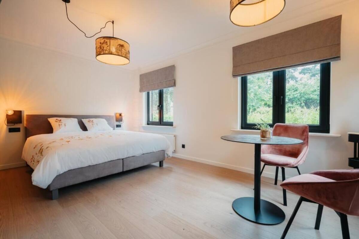 A bedroom with a bed, bedside tables, a round table with chairs, and large windows.