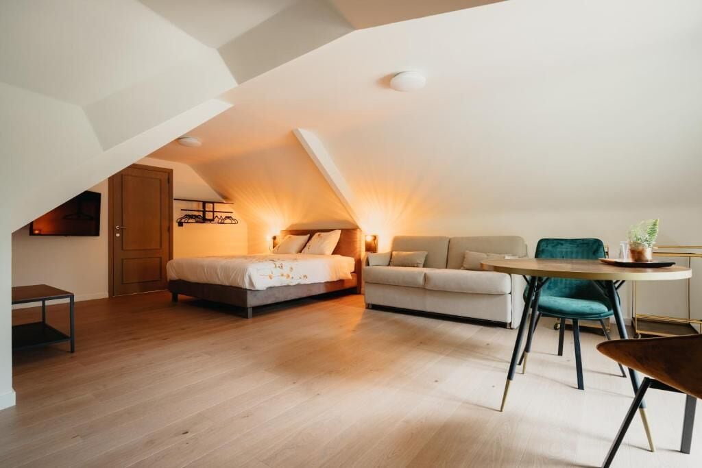 A loft-style bedroom with a bed, a sofa, a dining table, and a chair.