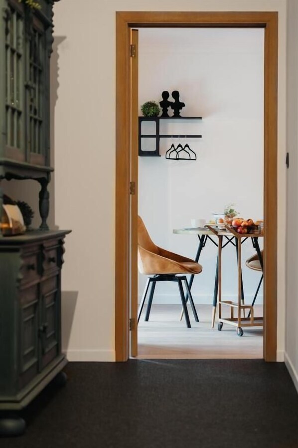 Un umbral que da a una habitación con un armario de madera, una silla, una mesita y estantes en la pared con objetos decorativos.